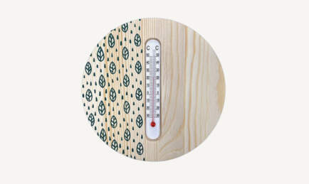 Thermomètre blanc sur un fond en bois rond avec un motif goutte d'eau sur la partie gauche.
