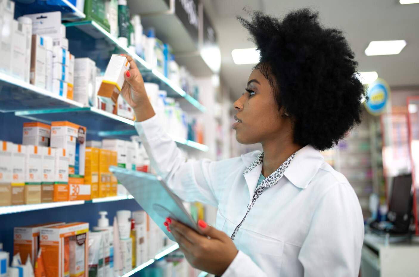 Pharmacienne en blouse dans son officine en train de préparer des produits pour un patient.