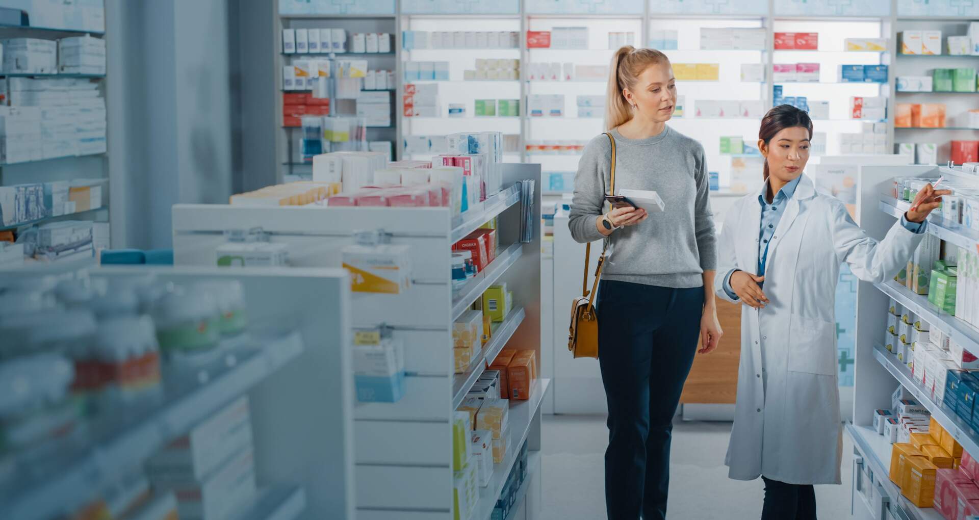 Une femme consulte les rayons de la pharmacie avec un professionnel de santé à ses côtés