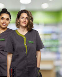 Deux femmes en blouses grises et vertes se trouvent dans une pharmacie